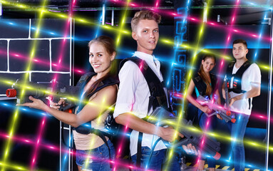 Fototapeta na wymiar Young guys and girls in vests holding plasticlaser pistols and p