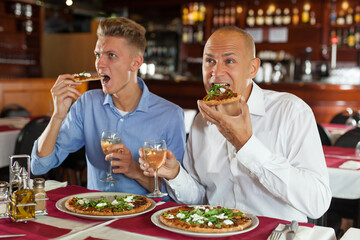 Male friends watching sport match and enjoying pizza in restaurant