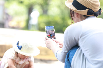 
砂場で遊ぶ子供をスマートフォンで撮影する母親