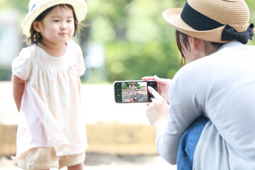 
砂場で遊ぶ子供をスマートフォンで撮影する母親