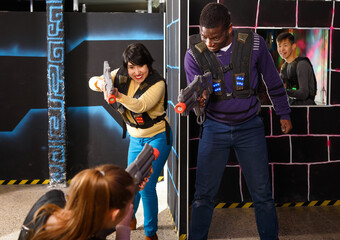 Modern people of different nationalities with laser pistols playing laser tag on dark labyrinth