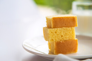 Close up stack of butter cake in a white plate on white table with a cup of milk blurred background.