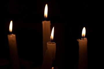 Burning candles on a dark background. The light of candles illuminates the darkness.