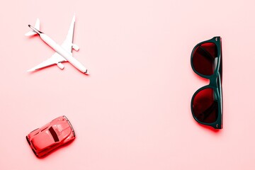 High plane toy in airplane travel concept. White aircraft, sunglasses and car on bright pink backdrop in top view. Aircraft on air sky background.