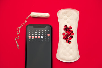 Menstrual cycle concept. Calendar for the month with marks in mobile application on the smartphone screen. Alarm, cotton tampon, sanitary pad, red sparkles on the red background.