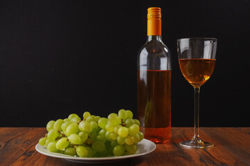 Fototapeta na wymiar Still life image. White wine and cluster of fresh juicy grapes on a white plate and glass of wine, Black background. Concept winery production.