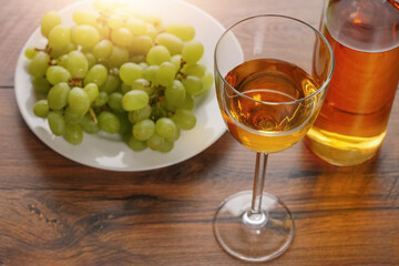 Glass of white wine in focus, Bottle of wine and cluster of fresh grapes on a white plate out of...