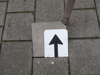 arrow on a brokne sign on a tile on the sidewalk
