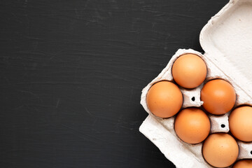 Raw Brown Eggs in a paper box on a black surface, top view. Flat lay, overhead, from above. Space for text.
