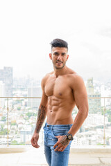 Fototapeta premium Happy young handsome muscular Persian man smiling shirtless against view the city