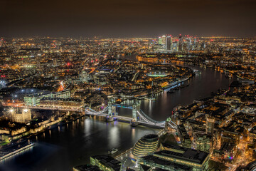 Aerial photograph of  London city and Tower Bridge and the River Thames at night showing city lights leading to Canary Wharf, London England. 