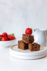 Fresh baked tasty chocolate brownies with strawberry and chocolate sauce on white marble background