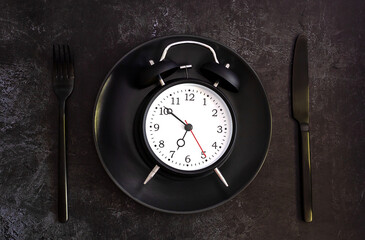 Black alarm clock on a black plate with black knife and fork. creative concept