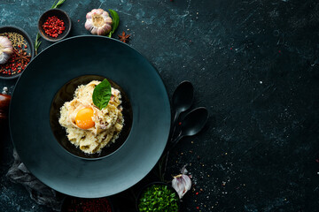 Carbonara pasta with egg and parmesan cheese and basil in a plate on a black stone background. Top view. Rustic style.