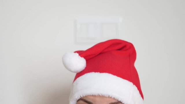 Caucasian woman puts on medical mask and santa christmas hat. Christmas celebration on lockdown