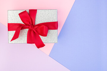 Silver glitter gift box with red ribbon on geometrical pattern made from pink, violet and blue paper, background for a template, horizontal, copy space