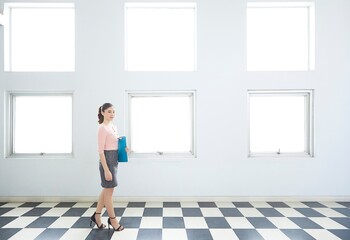 Young and pretty Asian business woman walking on the check pattern flooring.