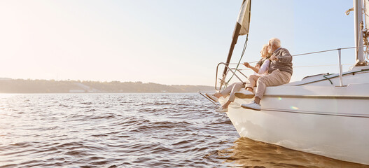 Explore dreams. A happy senior couple sitting on the side of a sail boat on a calm blue sea. Man...