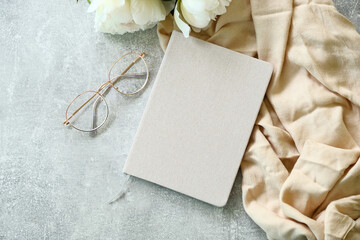 Flat lay paper notebook, eyeglasses, peony flowers and beige cloth on stone background. Top view...