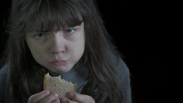 Poverty and bread. Hungry dirty little girl eats a piece of bread.