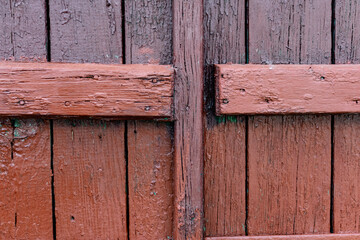 Wooden gates made of old painted red boards with a brown tinge and peeling texture. Simple vintage background and texture