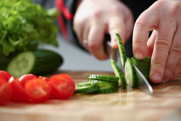 Close up of male chef hands slicing juicy vegetable for salad on wooden cutting board