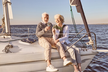 Happy senior couple sitting on the side of sail boat or yacht deck floating in sea. Man and woman...