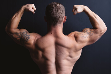 young bodybuilder with a short haircut stands near a black wall. concept: body parts, broad back of...