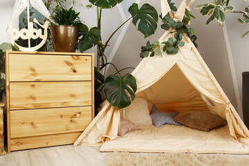 interior of a children's room or recreation area: a wigwam with soft pillows, a wooden nightstand made of environmentally friendly materials. plastic plants to decorate the space © skeronov