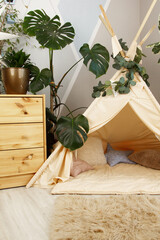 interior of a children's room or recreation area: a wigwam with soft pillows, a wooden nightstand made of environmentally friendly materials. plastic plants to decorate the space © skeronov