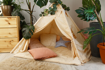 interior of a children's room or recreation area: a wigwam with soft pillows, a wooden nightstand made of environmentally friendly materials. plastic plants to decorate the space © skeronov