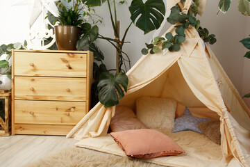 interior of a children's room or recreation area: a wigwam with soft pillows, a wooden nightstand made of environmentally friendly materials. plastic plants to decorate the space © skeronov