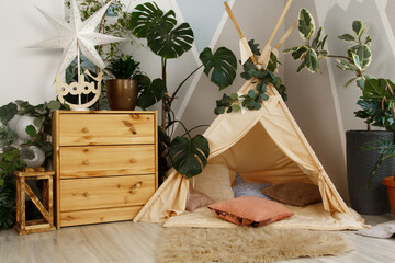 interior of a children's room or recreation area: a wigwam with soft pillows, a wooden nightstand made of environmentally friendly materials. plastic plants to decorate the space