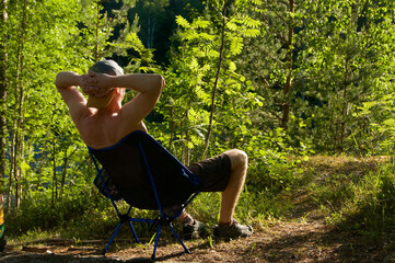Man sitting on camping chair in the forest. Outdoor recreation. People sitting in the forest. Carefree concept 