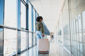 Young african american female passanger in casual clothes is in airport with baggage. Using phone. Travel concept