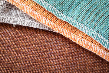 Fabric texture, sewn edges with white thread. Brown, grey, orange and turquoise color