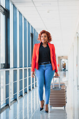 Young african american female passanger in casual clothes is in airport with baggage.