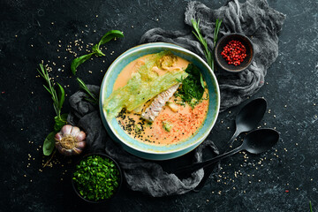 Seafood soup. Creamy tuna soup in a bowl on a black stone background. Top view. Rustic style.