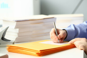 Close up of young man sitting at the table with documents and preparing corporate mail at work