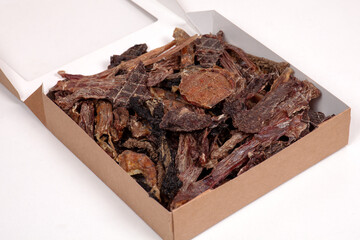 Opened craft cardboard box with dehydrated dog treats, full of dry meat crunchy tastes from beef and chicken. Homemade pet food, healthy and natural. Copy space.