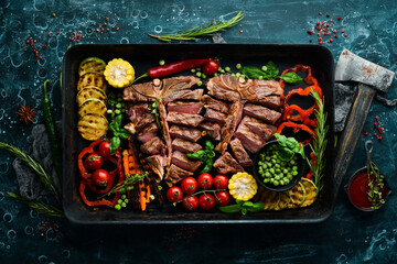 Sliced steak on the bone with grilled vegetables and spices. T-bone steak. Top view. Rustic style.