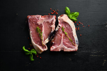 Dry raw two T-bone steak on the bone with spices on a black stone background. Top view. Rustic...