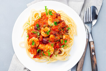 Italian dish shrimp linguine Puttanesca, pasta with shrimps in spicy tomato basil sauce garnished with parsley, on white plate, horizontal, top view