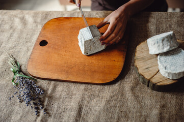 Valencay cheese on a wooden board. Cheesemaker cuts cheese with blue mold, close-up. French soft...