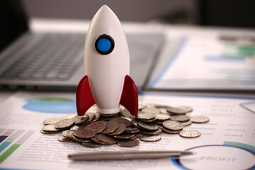 Close up of toy spacecraft and scattered coins on table with documents and laptop