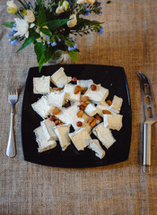 Camembert, French soft cheese with white mold and traditional French goat Valencay cheese cut into pieces and decorated with almonds on a black plate. Cheese plate. Film noise