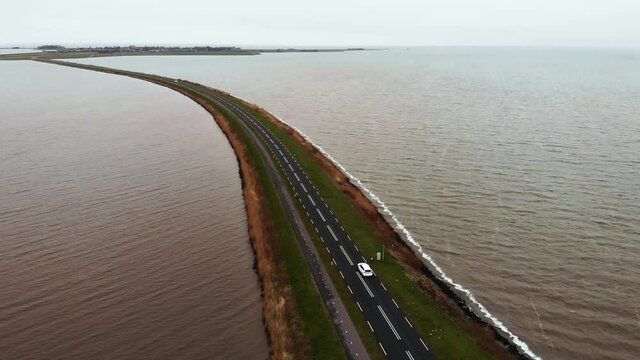 Aerial Flyby shot of White car moving by the Highway Road on the Dam in Netherlands connecting Mainland with a Marken island in Holland