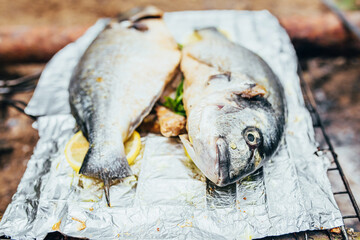 Two dorado fish on foil in marinade and with lemon before frying