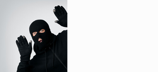 Masked thief with raised arms isolated on white wall