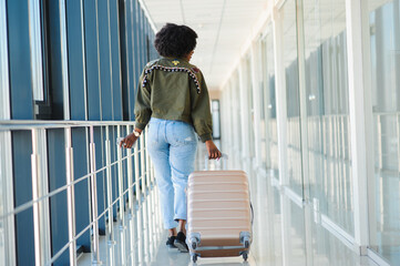 Young african american female passanger in casual clothes is in airport with baggage.